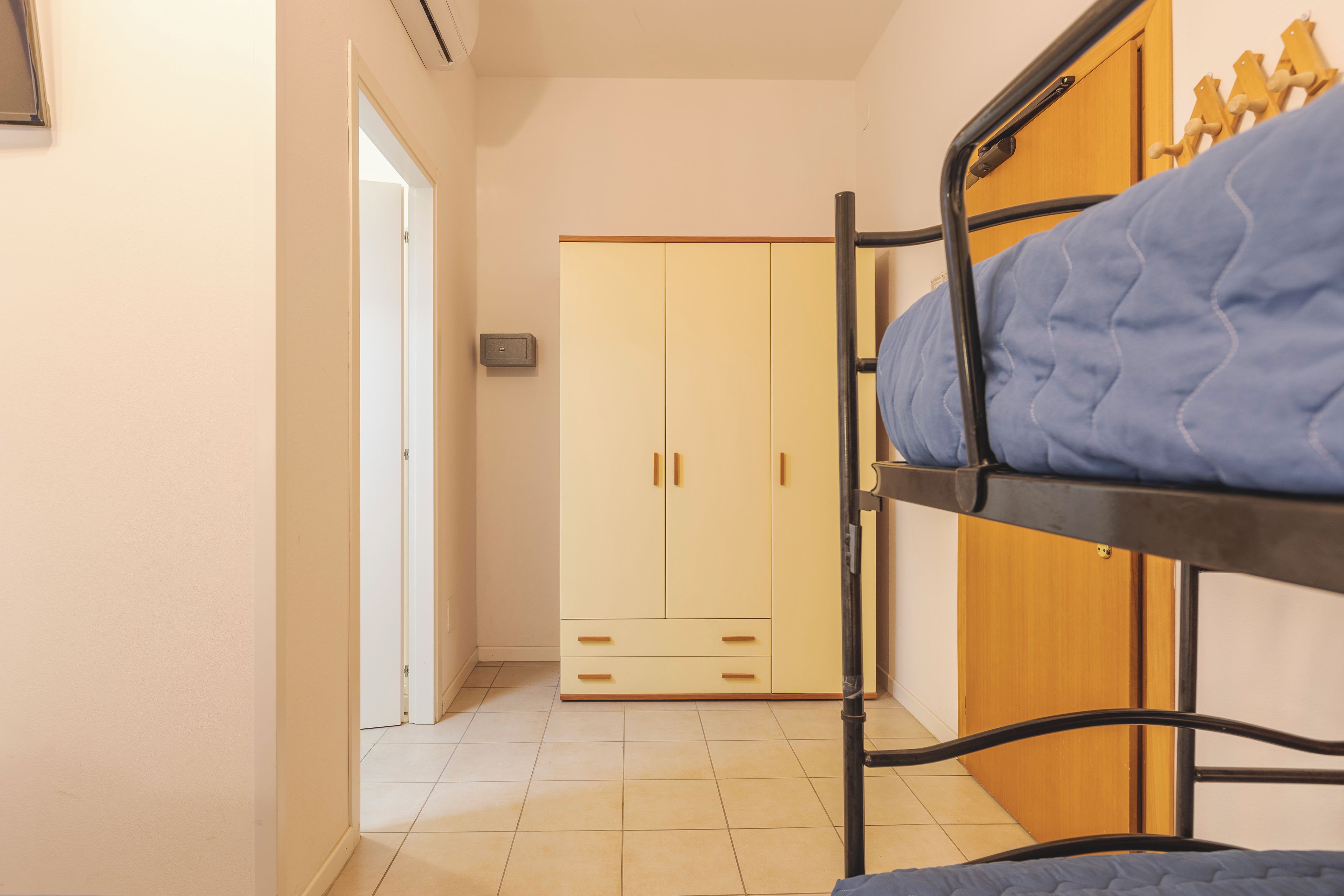 A room with a bunk bed, a wardrobe, and a door leading to another room.