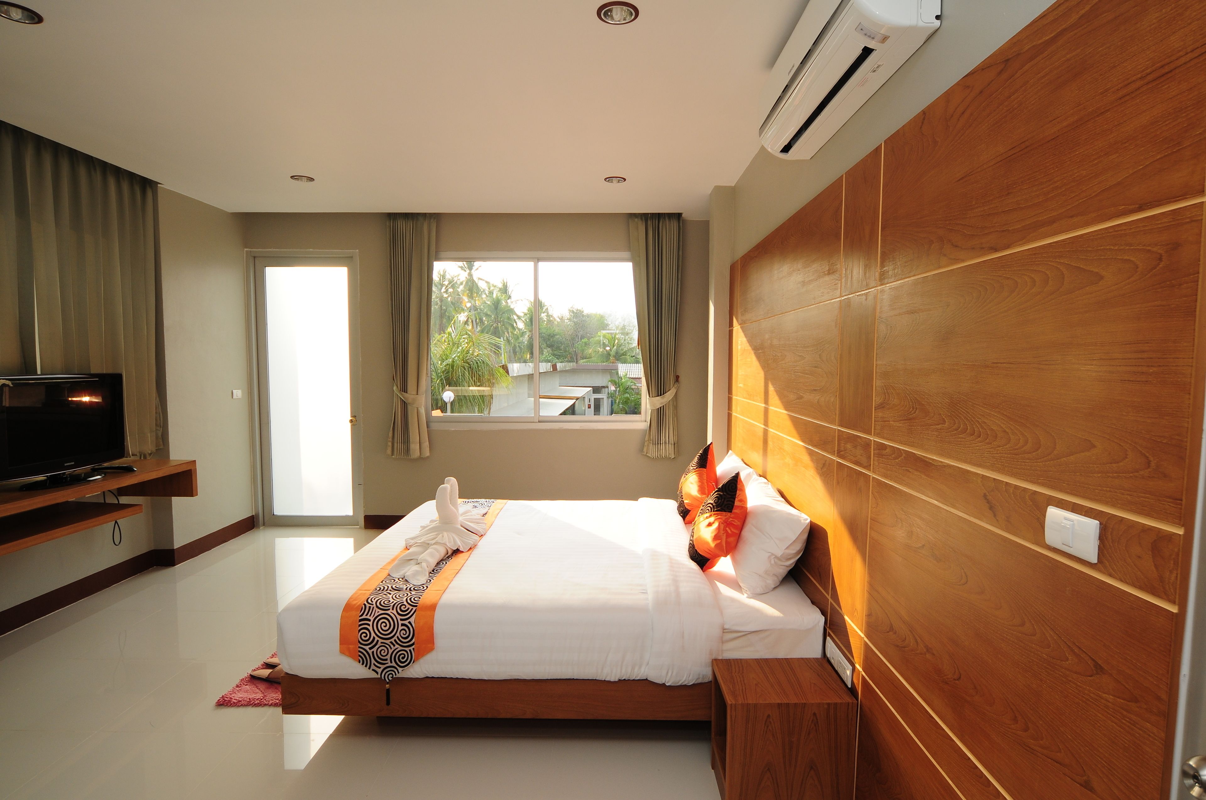 A hotel room with a bed, a TV, a wooden headboard, and a window with curtains.