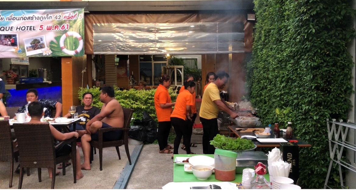 Un'area pranzo all'aperto con tavoli, sedie, un angolo barbecue e un muro verde.