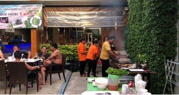 Un'area pranzo all'aperto con tavoli, sedie, un angolo barbecue e un muro verde.