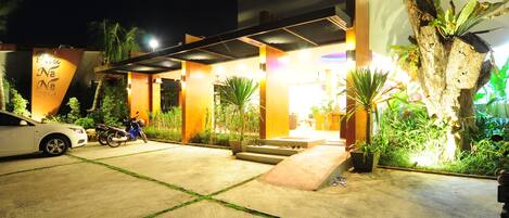 A well-lit hotel entrance with a covered outdoor area, a car, and a motorcycle parked in the driveway.