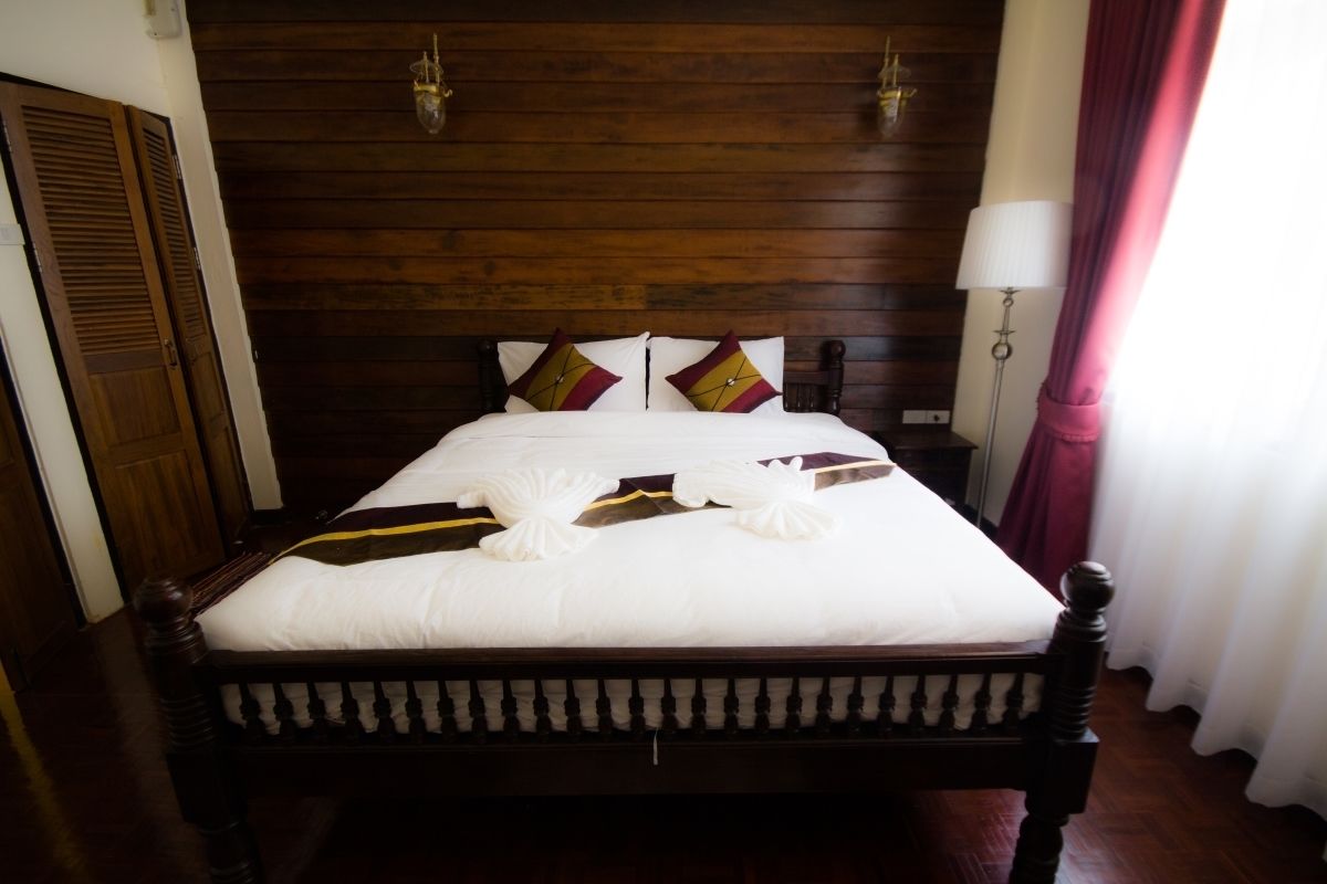 A neatly made bed with white linens and decorative pillows, a wooden headboard, and a nightstand with a lamp.
