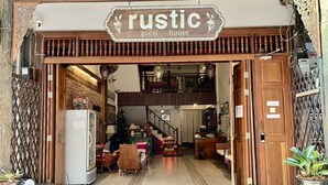 A rustic guest house with a wooden entrance, a staircase leading to an upper level, and a cozy interior with furniture and plants. - Rustic Guesthouse (Chiang Mai)