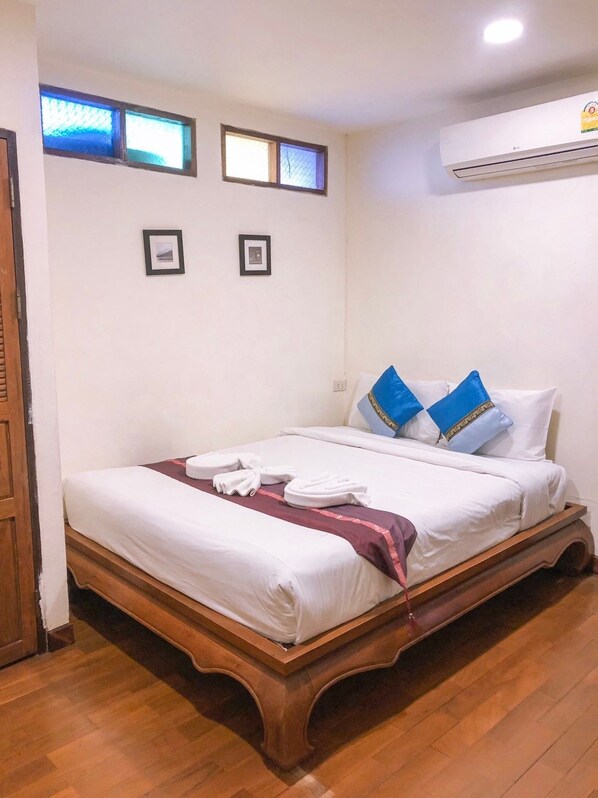 A neatly made bed with white linens and a maroon throw, two pillows with blue and gold accents, and a wooden headboard. - Rustic Guesthouse (Chiang Mai)