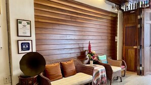 A room with a wooden slatted wall, a sofa, a small table with a striped tablecloth, and a decorative vase with flowers. - Rustic Guesthouse (Chiang Mai)