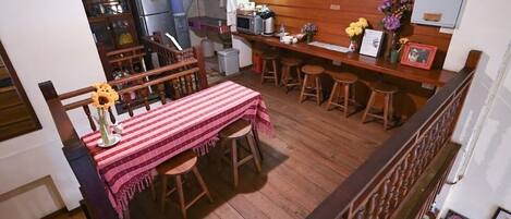 A dining area with a wooden table and chairs, a kitchen in the background, and a small bar area with stools.
