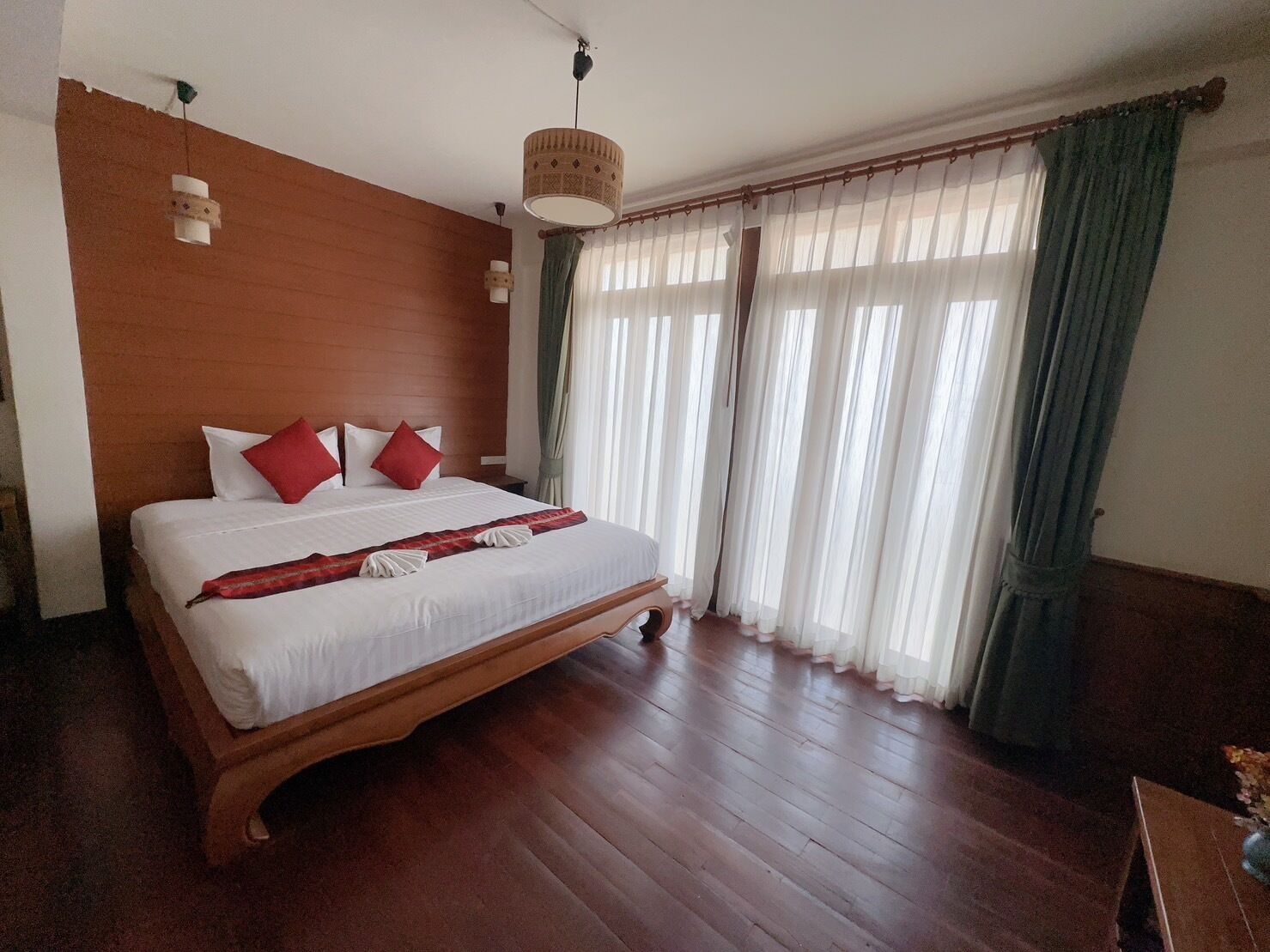 A large bed with white linens and red pillows, wooden headboard, and a wooden floor.
