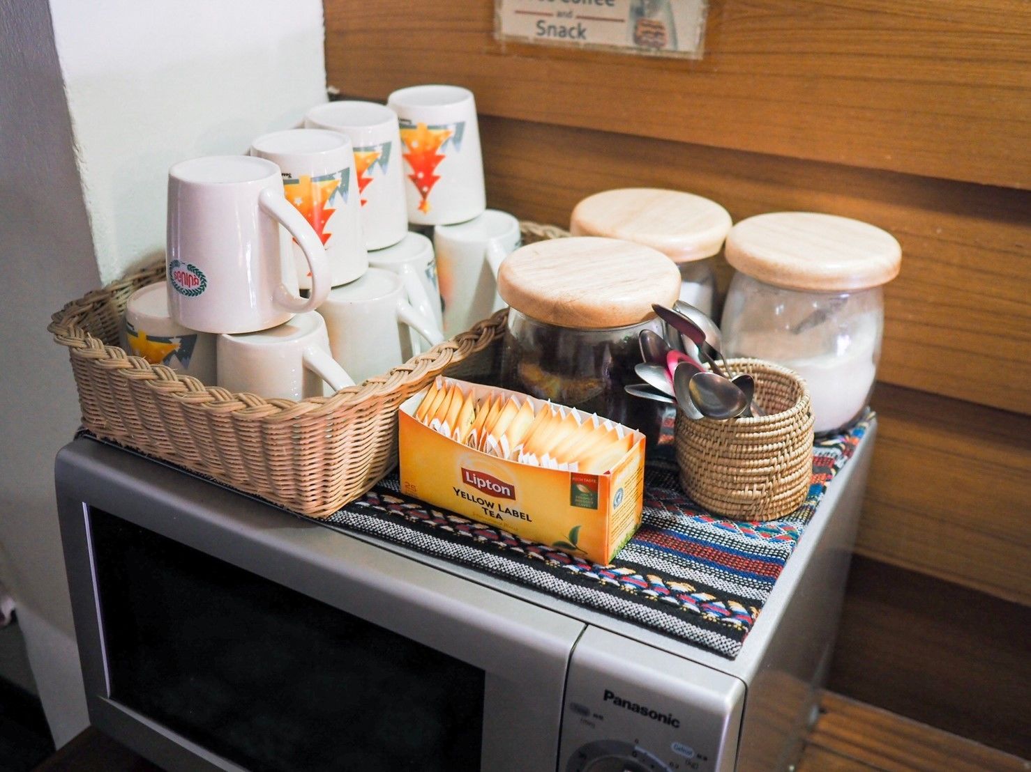 A microwave with a basket of bread, a box of Lipton tea, and several mugs and jars on top.
