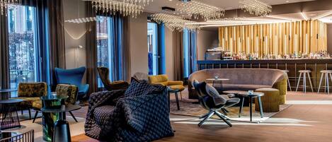 Eine moderne Hotelhalle mit verschiedenen Sitzbereichen, einer Bar und großen Fenstern mit Blick auf die Stadt.