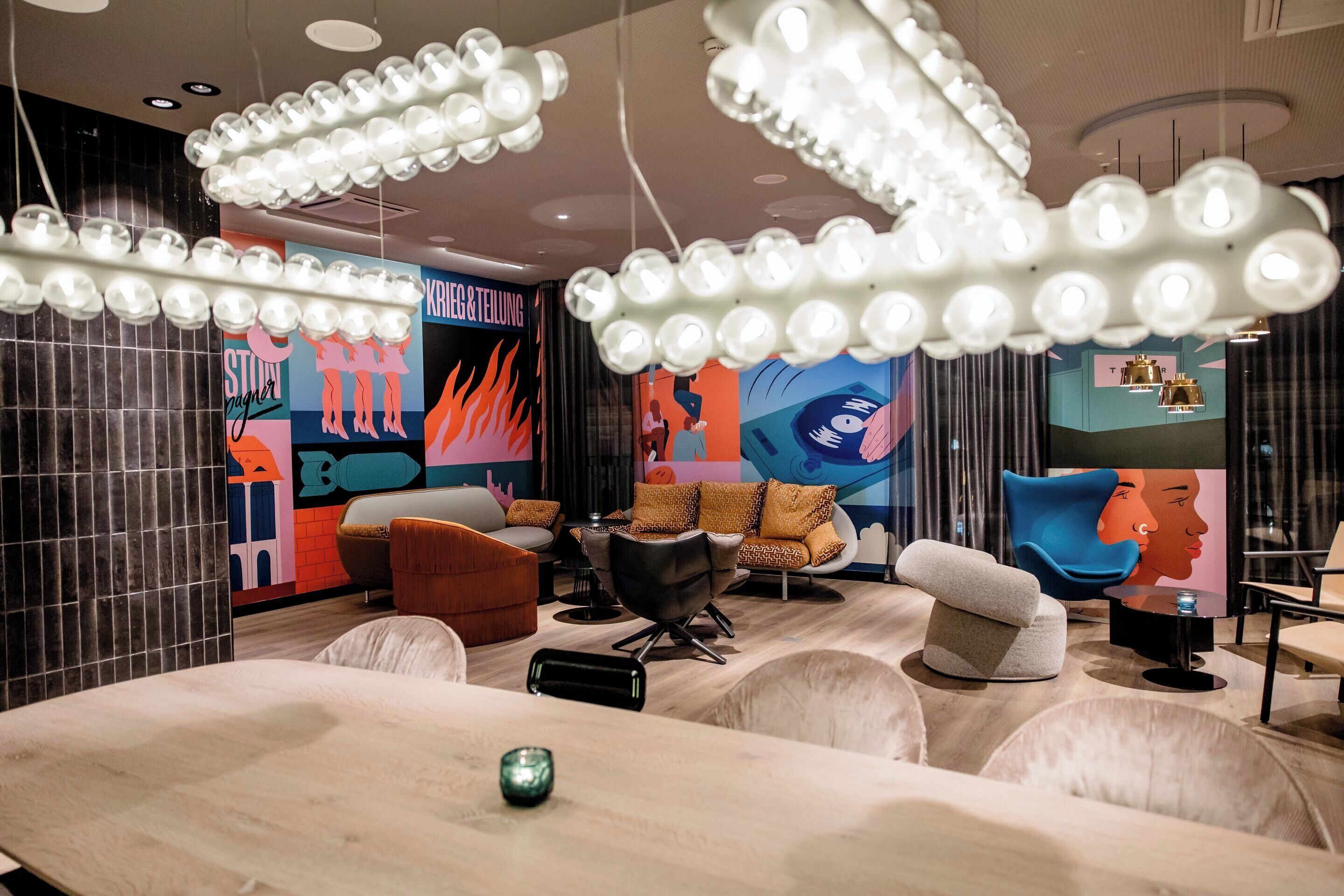 A modern interior with a large table, multiple seating areas, and a wall with colorful artwork.