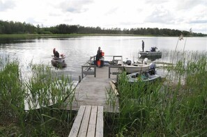 A wooden dock extending into a calm lake with boats and people. - Brovillan (Lekeryd)