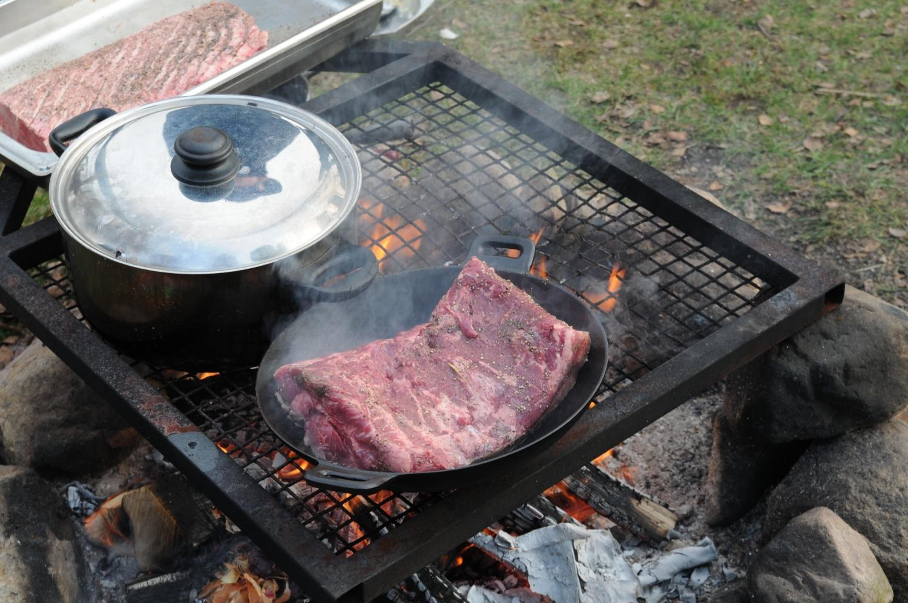 Un gril avec une casserole et un steak en train de cuire sur une flamme nue.