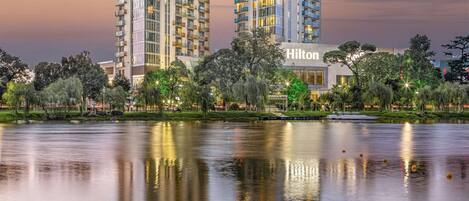 A high-rise hotel with a glass facade, located beside a body of water with reflections.