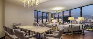 A modern dining area with a large table and chairs, a sofa, and a TV. There are large windows with a city view. - Hilton Batumi (Batumi)