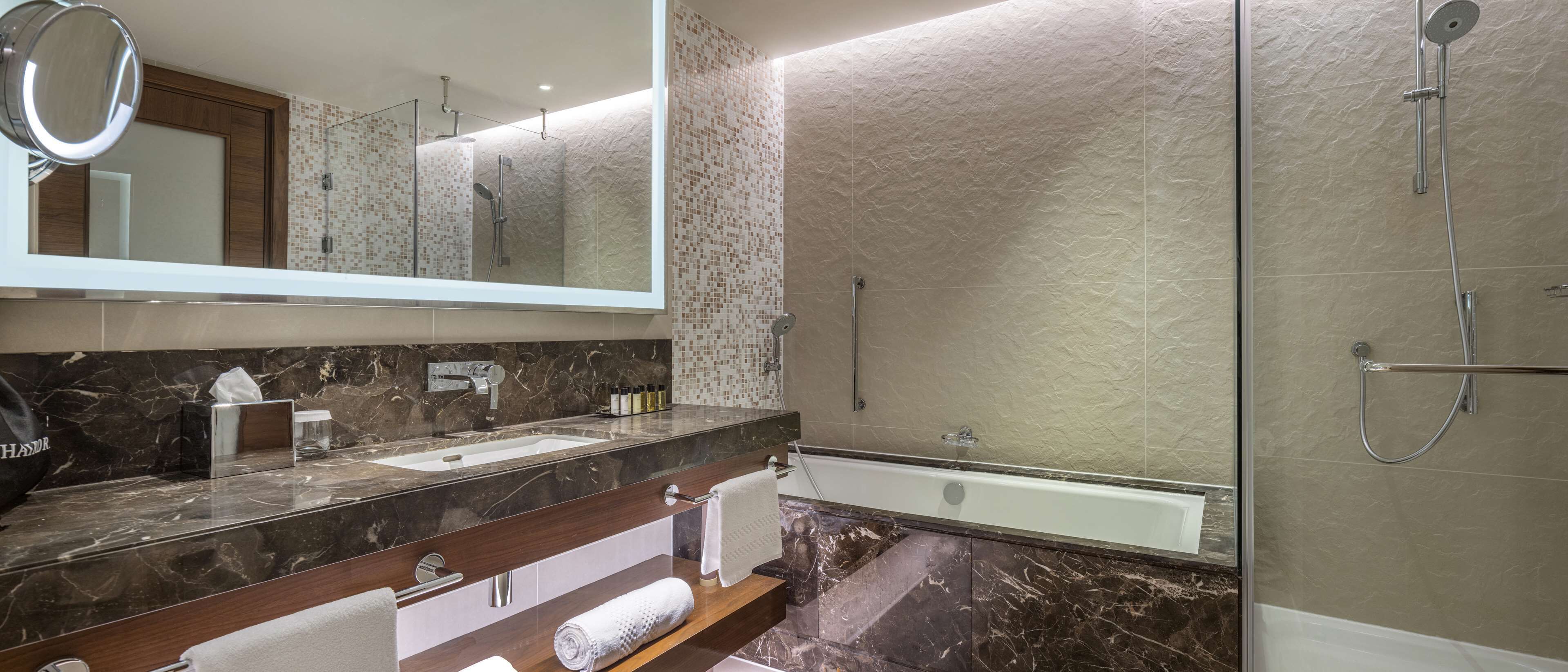 A modern bathroom with a large mirror, two sinks, a bathtub, and a glass-enclosed shower.