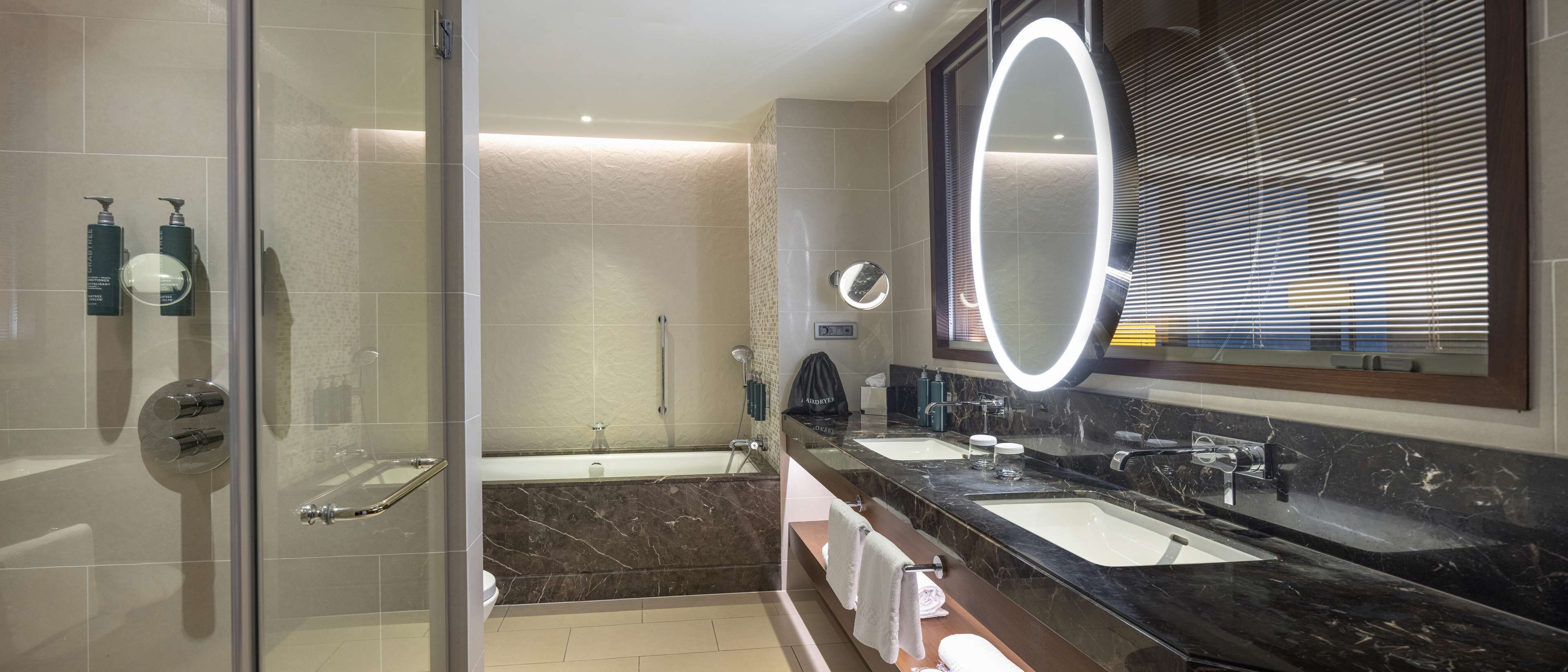 A modern bathroom with a glass shower enclosure, a separate bathtub, and a vanity with dual sinks and a large mirror.