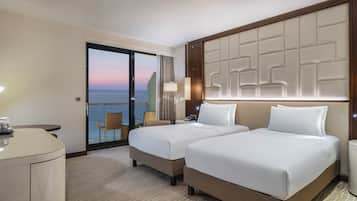 Habitación de hotel con dos camas, un escritorio, un minibar y vista al mar.
