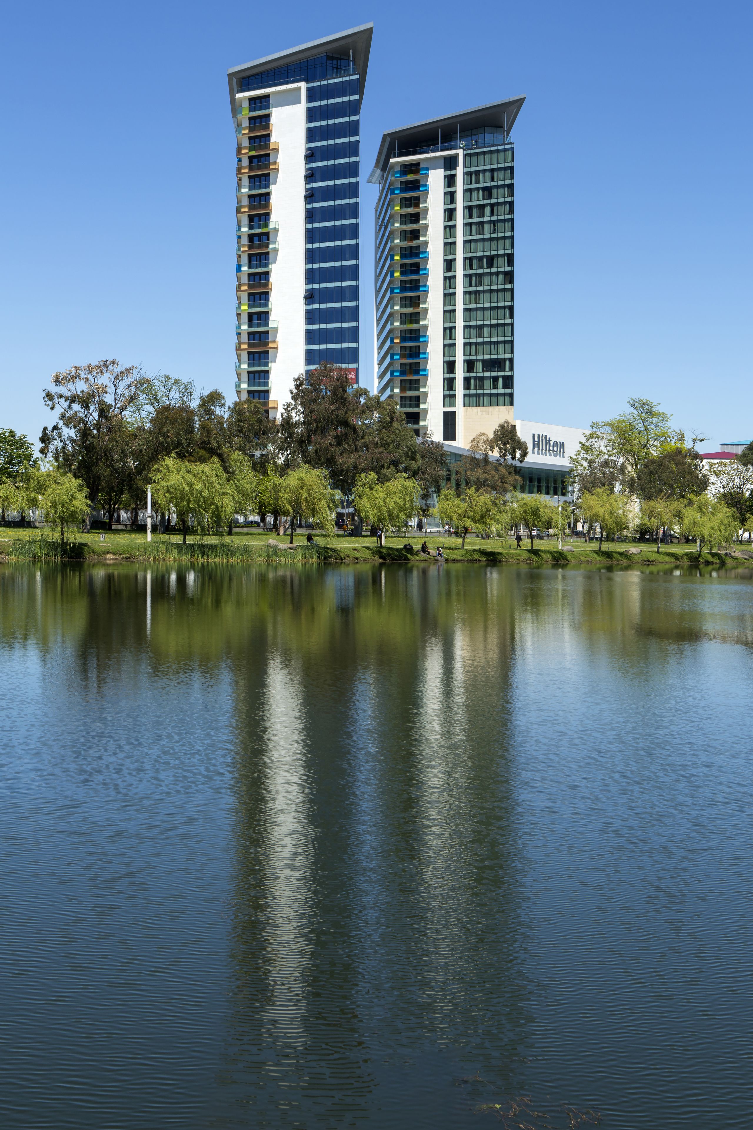 Un hotel Hilton de diseño moderno, con una gran extensión de agua al frente y un parque con árboles.
