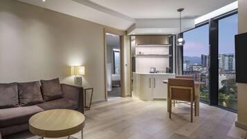 A modern living room with a sofa, a round coffee table, and a view of a cityscape through large windows.