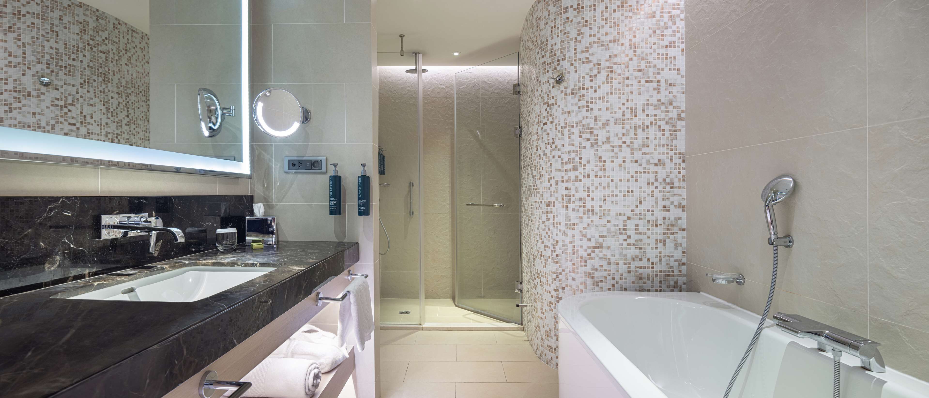 A modern bathroom with a large mirror, two sinks, a shower, and a bathtub.