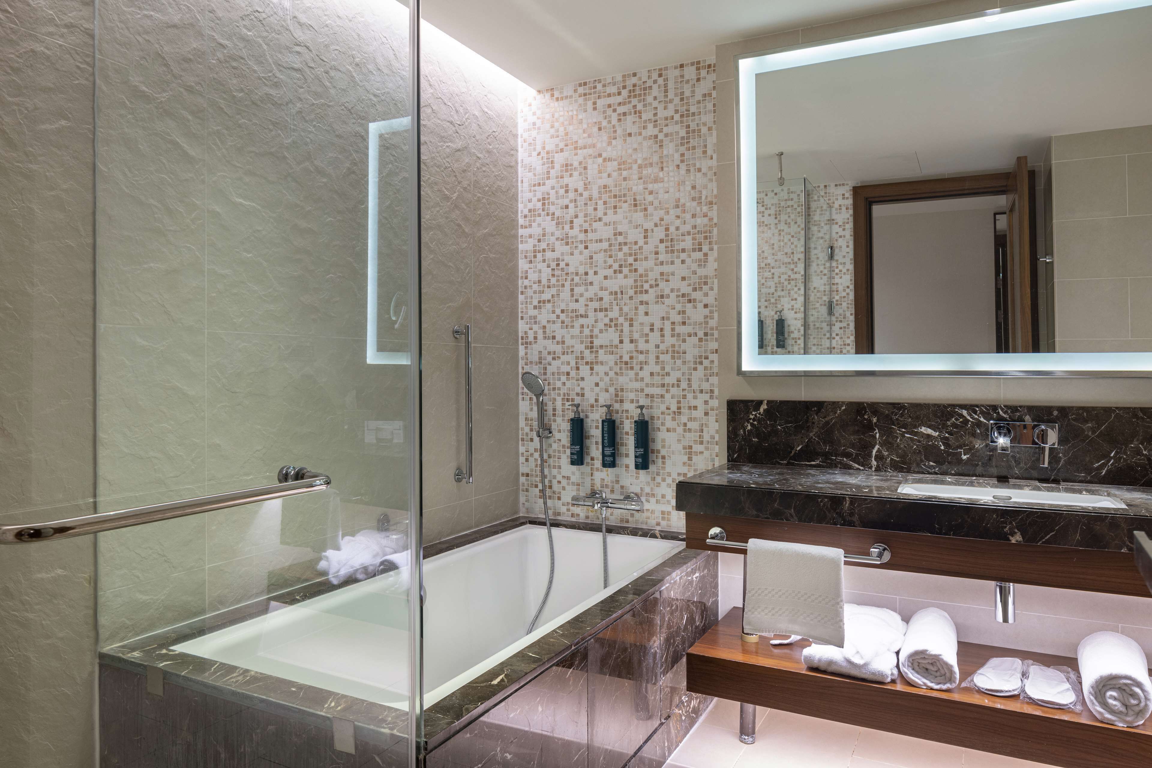 Un baño moderno con ducha envuelta en vidrio, encimera de mármol y un espejo grande.