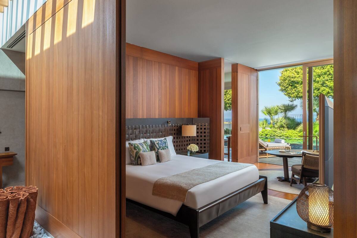 A modern hotel room with a large bed, wooden paneling, a desk, and a view of the outdoors.