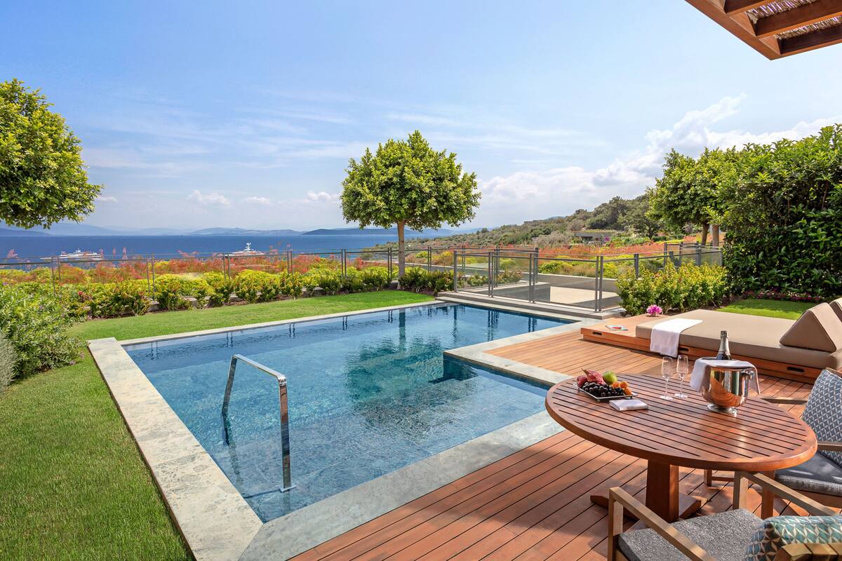 A swimming pool with a wooden deck, outdoor seating, and a view of the sea.