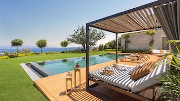 Un área de estar moderna al aire libre con piscina, terraza de madera y vista al mar.