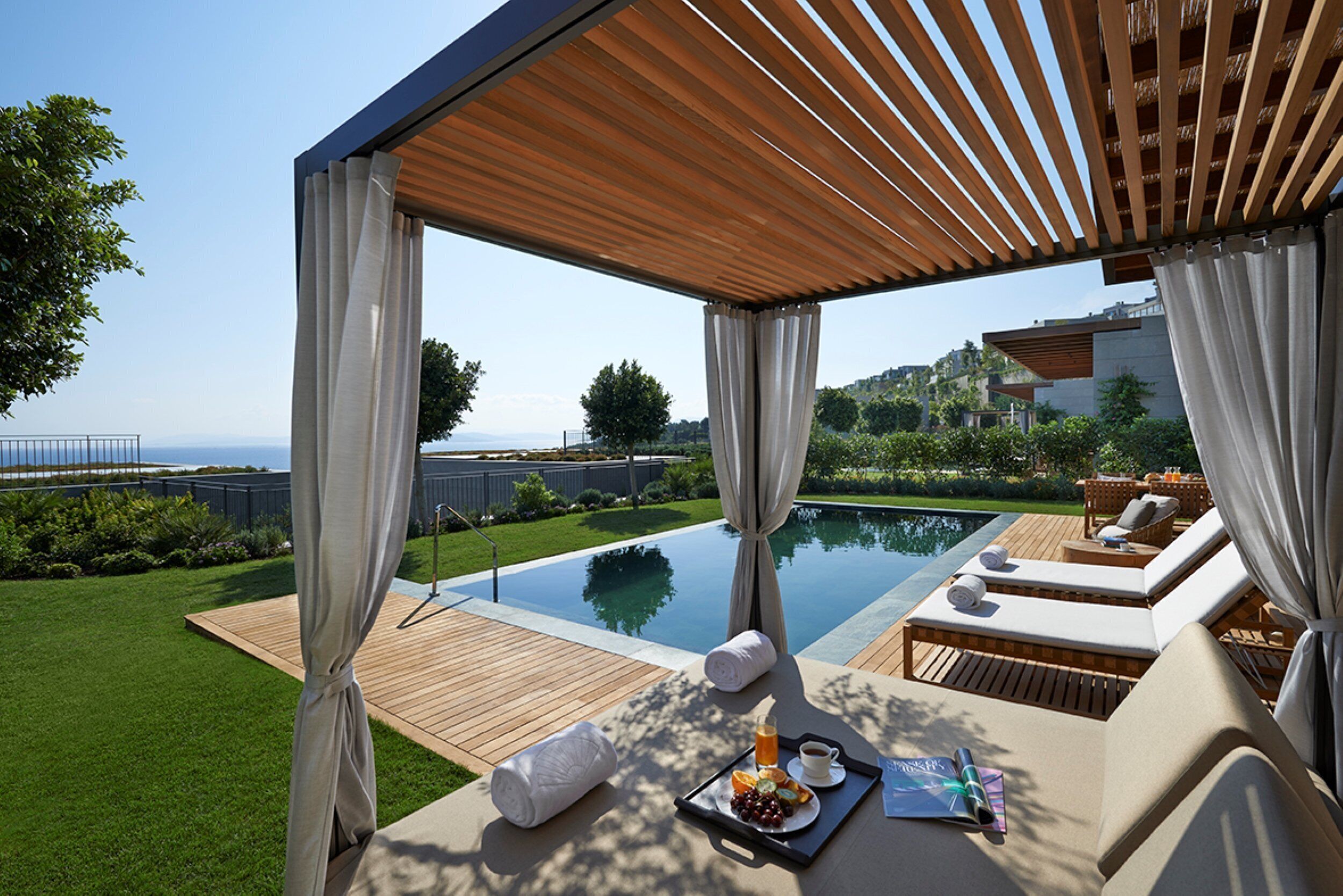Un entorno exterior lujoso con piscina, tumbonas y una pérgola de madera.