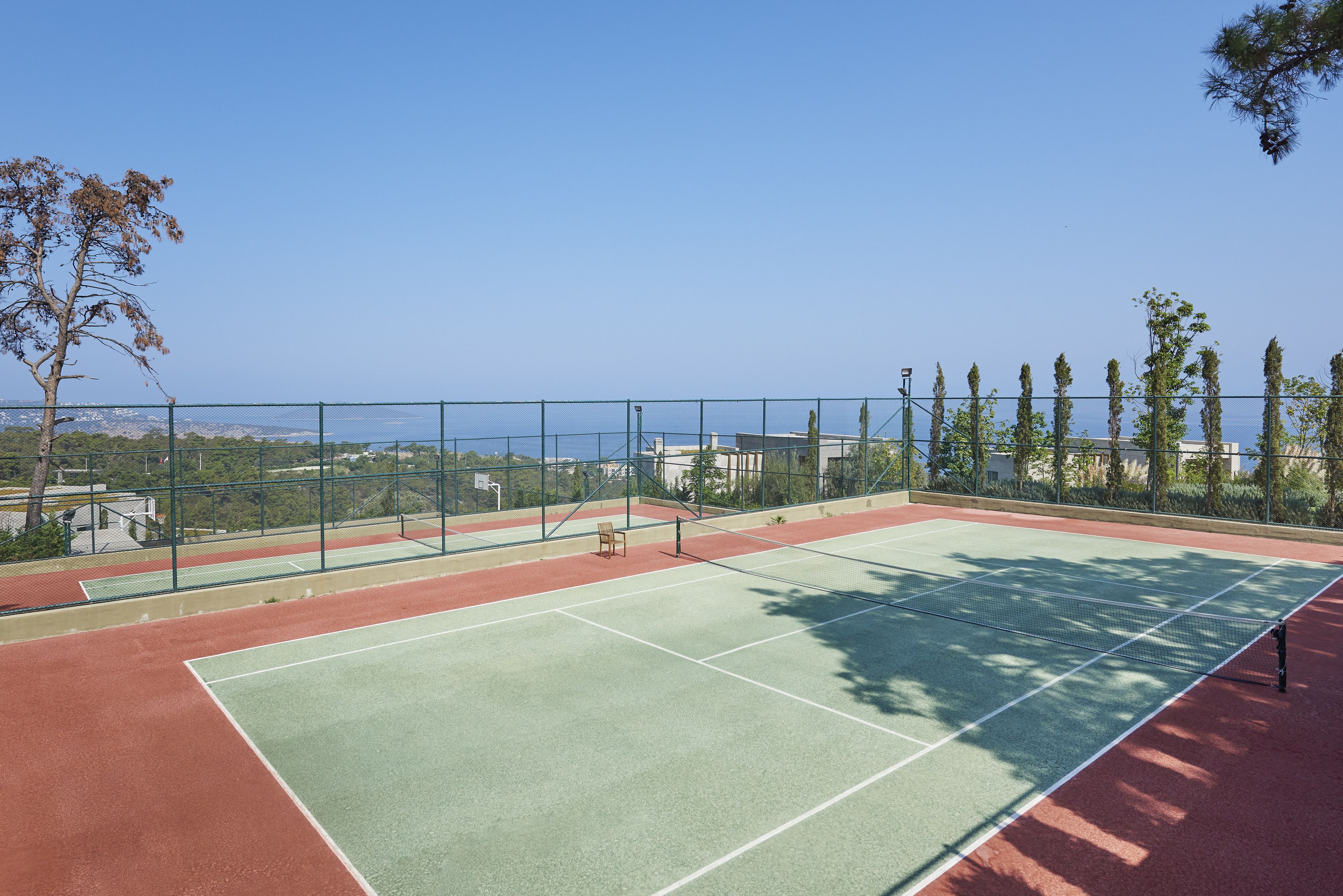 An outdoor tennis court with a clear view of the surrounding landscape, including trees and buildings.