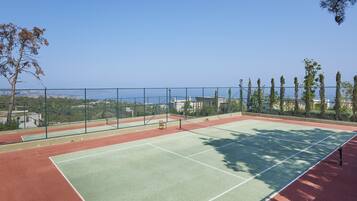 An outdoor tennis court with a clear view of the surrounding landscape, including trees and buildings.
