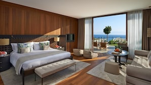 Una habitación de hotel moderna con una cama grande, una zona de estar con una mesa y un balcón con vistas al mar.