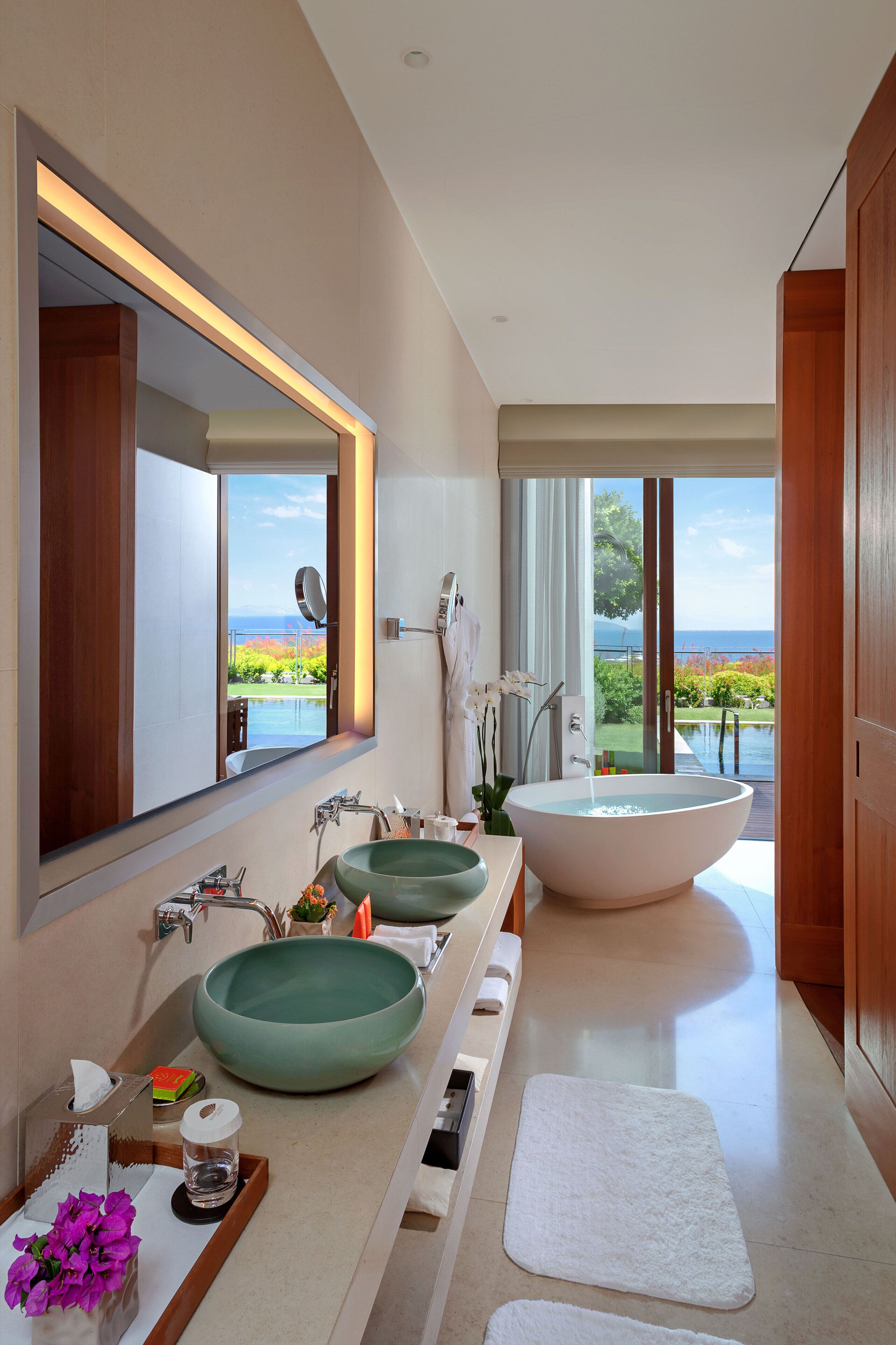 A modern bathroom with a large bathtub, two sinks, and a view of the ocean.