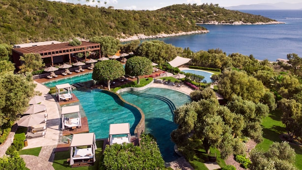 Vista aérea de un complejo turístico con una gran piscina, zonas de descanso y vistas al mar.