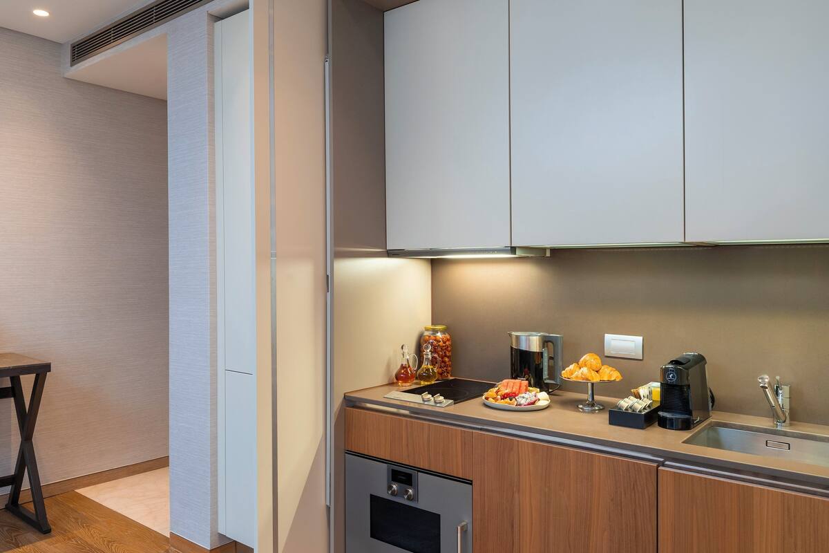 A modern kitchen with a built-in oven, a sink, and a countertop with various items including a coffee maker, a jar of jam, and a plate of food.