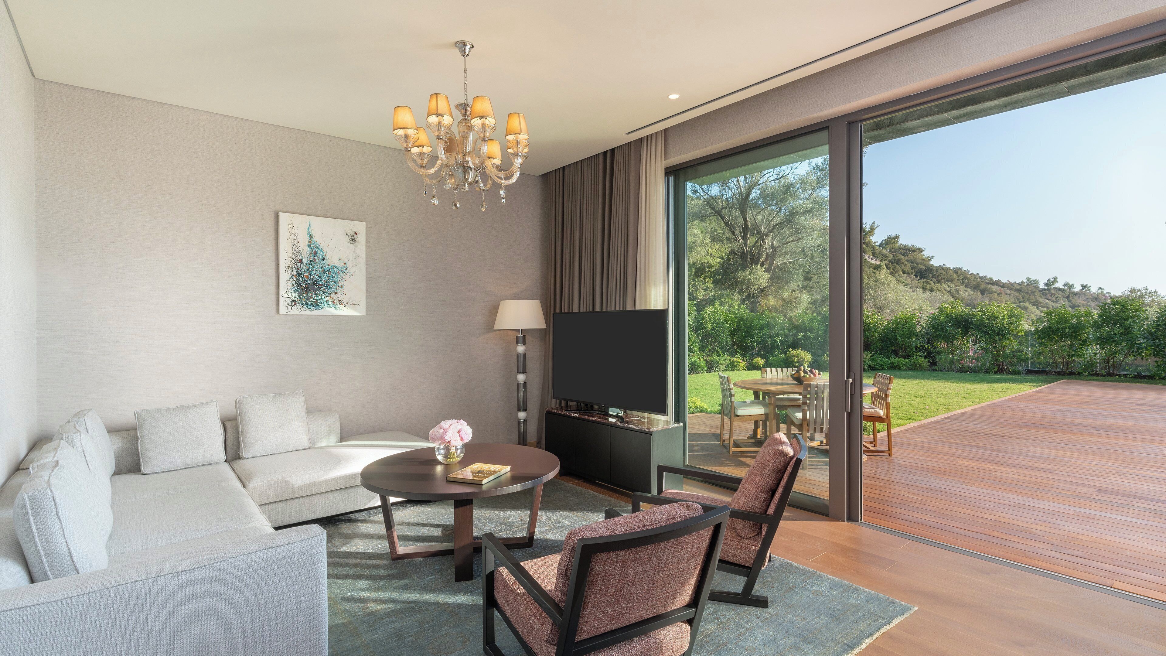 Un salon moderne comprenant un canapé, une table basse et des fauteuils, un tél éviseur à écran plat et une grande porte-fenêtre coulissante donnant sur une terrasse extérieure.