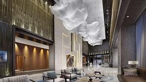 Um hall espaçoso com assentos modernos, uma grande escultura abstrata e teto alto com elementos pendentes.