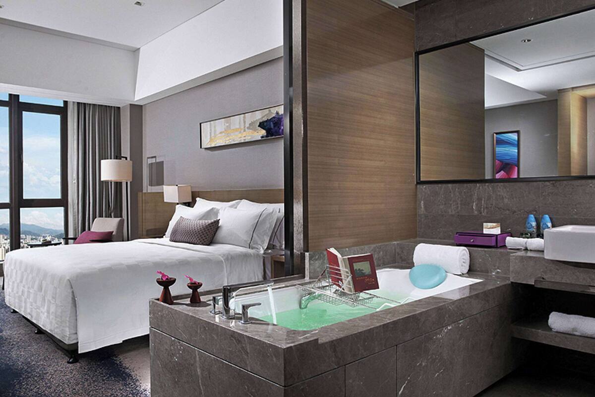 A modern hotel room with a large bed, a bathroom with a marble sink, and a city view.