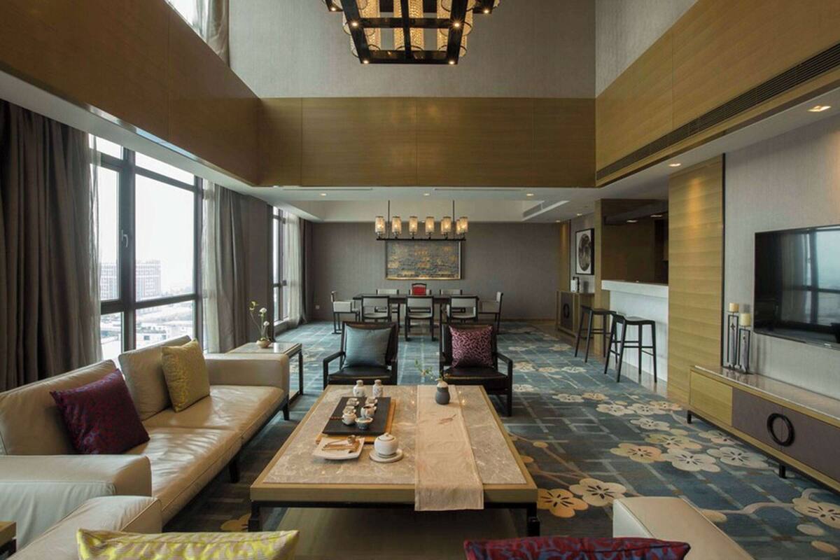 A spacious hotel living room with a sofa, coffee table, dining area, and a TV.