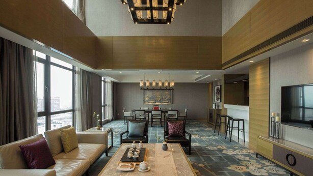 A spacious hotel living room with a sofa, coffee table, dining area, and a TV. - Wyndham Jinjiang (Quanzhou)