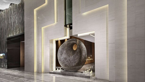 Um lobby moderno com uma grande escultura de pedra, designs geométricos nas paredes e piso de mármore polido.