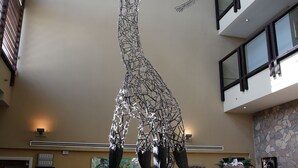 A sculpture of a giraffe in a lobby with a stone fireplace and a penguin display. - Chessington Resort Hotel (Chessington)