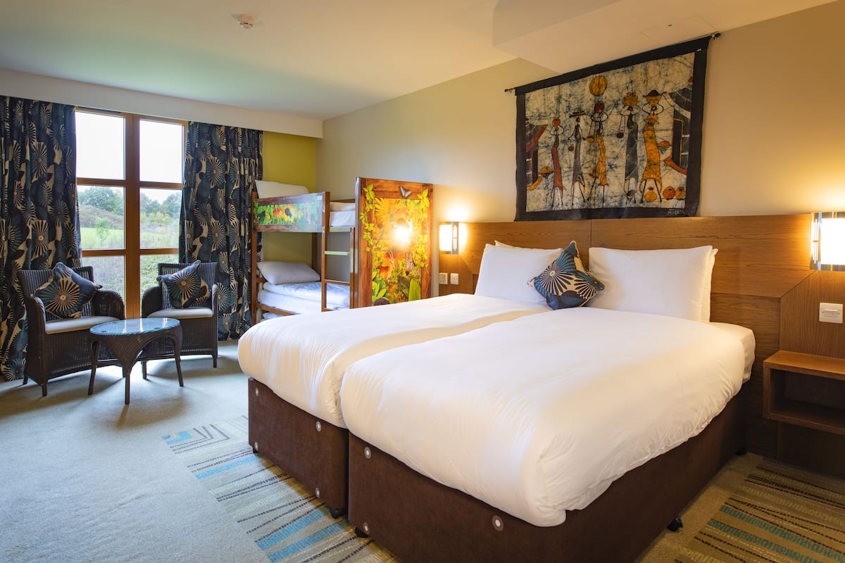 A hotel room with a large bed, a sofa, a small table, and a window with curtains.