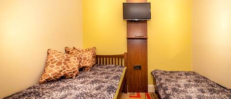 Una habitación pequeña con dos camas, cada una con una colcha de estilo leopardo, un cabecero de madera y un televisor montado en la pared.