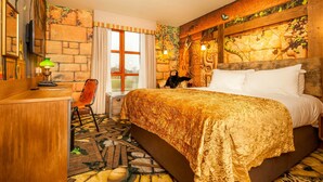 A hotel room with a large bed, a desk, and a chair. There is a window with curtains, a wall with a stone pattern, and a wall with a wooden beam and leaves. - Chessington Resort Hotel (Chessington)