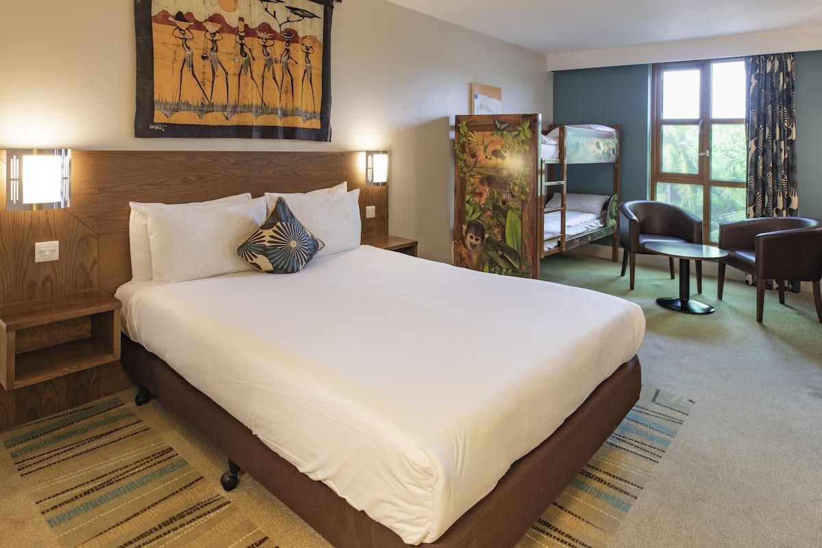 A hotel room with a large bed, a desk, a chair, a window with curtains, and a painting on the wall.