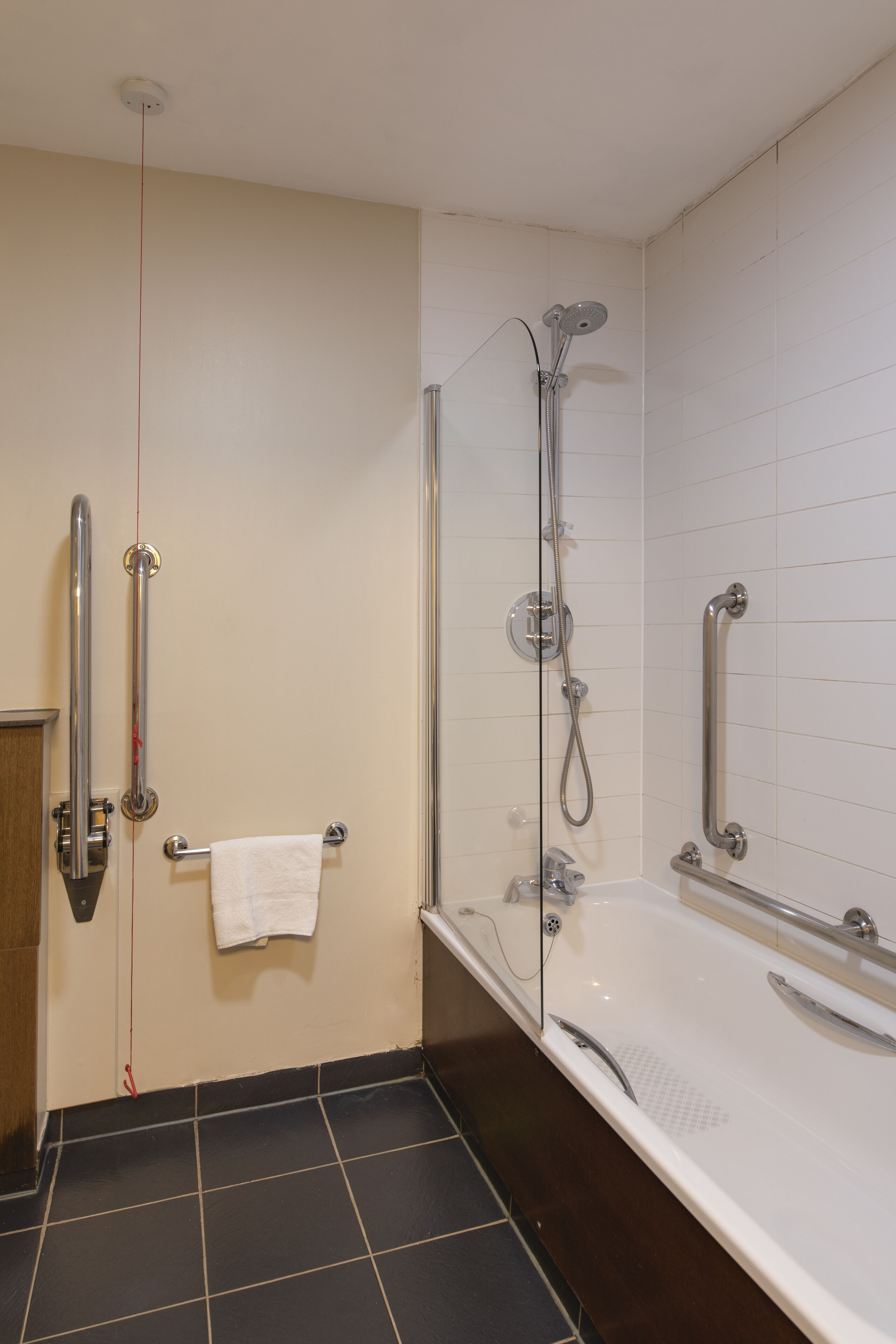 A bathroom with a walk-in shower, grab bars, a white bathtub, and a towel hanging on the wall.