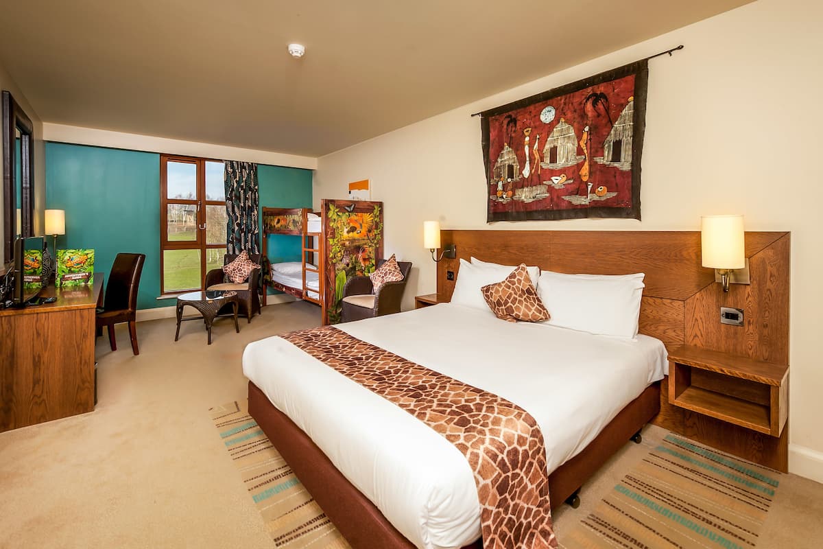 A hotel room with a large bed, a desk, a chair, a wardrobe, and a painting on the wall.