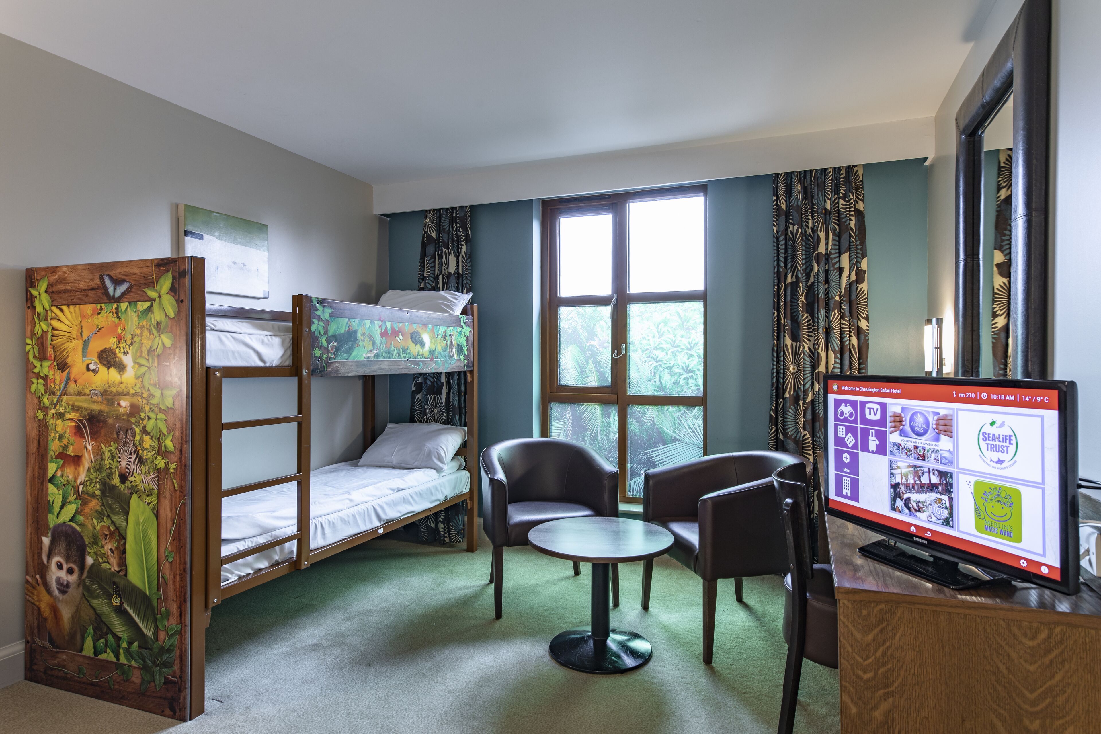 A room with bunk beds, a desk with a computer, two chairs, and a window with curtains.