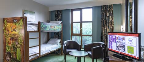 A room with bunk beds, a desk with a computer, two chairs, and a window with curtains.